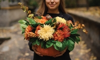 A woman holds a pumpkin full of flowers. 