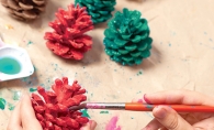 A person paints pinecones red and green.