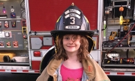 A girl at National Night Out in Maple Grove wears equipment from the Maple Grove Fire Department