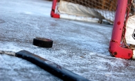 A hockey stick and puck rest in front of the net on an ice rink in Maple Grove.