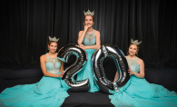 Three Maple Grove ambassadors in blue dresses hold a silver "20" balloon.