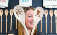 A woman holds two wooden serving spoons with a Minnesota theme from The Vintage Studio
