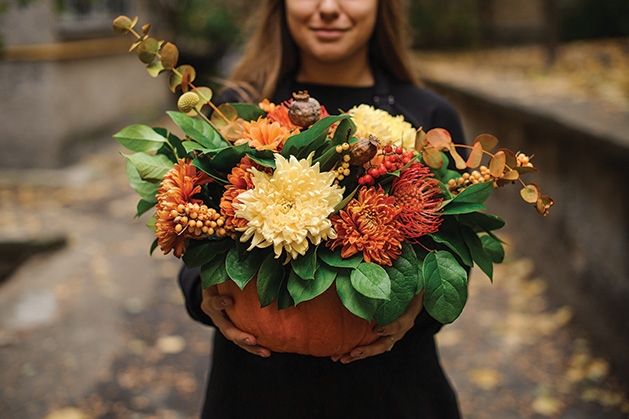 A woman holds a pumpkin full of flowers. 