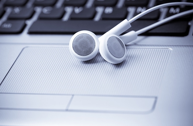 A pair of white headphones sit on a computer keyboard.