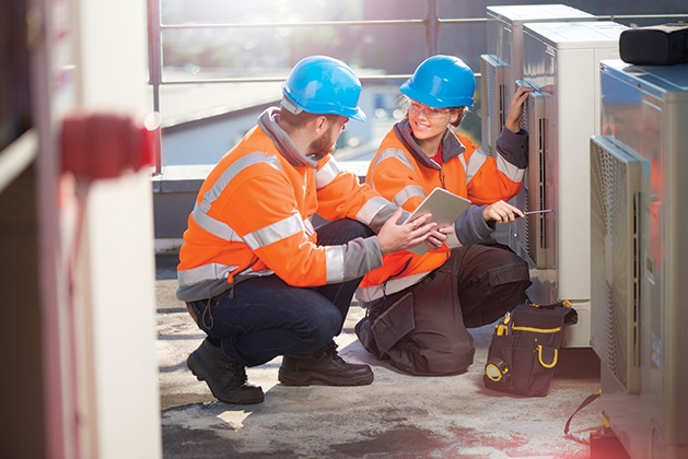 Two HVAC technicians work on a unit.