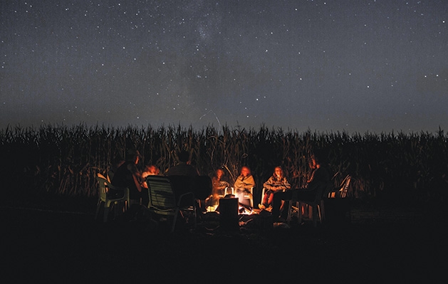 A group of kids sit around a campfire telling scary stories.