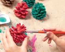 A person paints pinecones red and green.