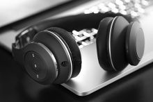 In this black and white photo, a pair of wireless headphones rests on a laptop.