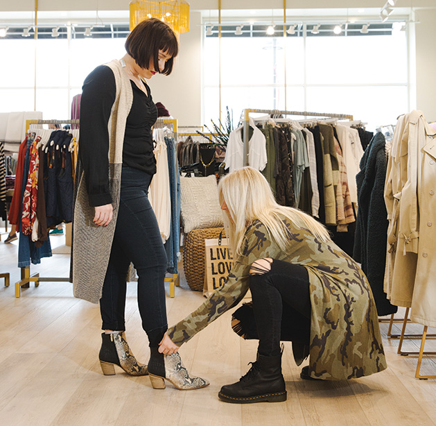 A stylist at leela & lavender helps a woman try on a pair of boots.