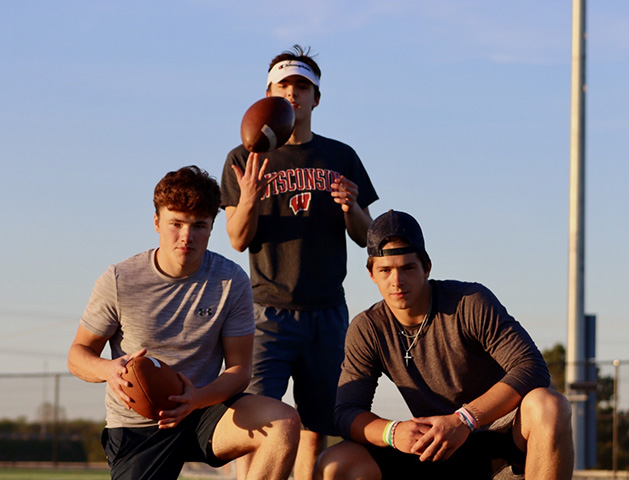 Three teenage boys pose with footballs.