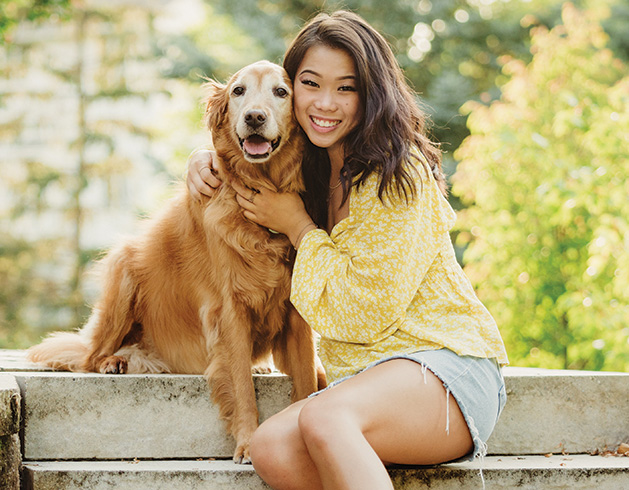 A girl poses with her dog for a senior picture taken by Any Angle Photography